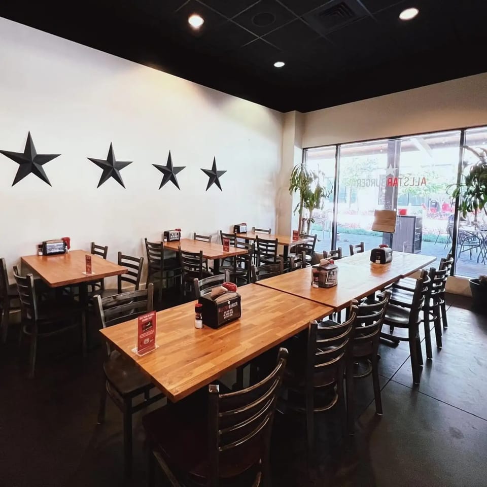 Interior of a restaurant with wooden tables, dark chairs, and large windows, featuring five black stars on a white wall.
