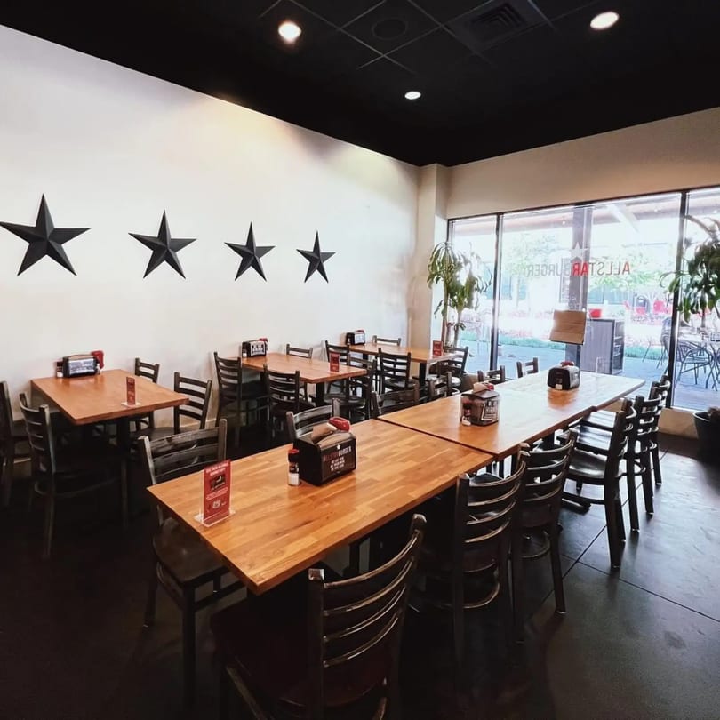 Interior of a restaurant with wooden tables, dark chairs, and large windows, featuring five black stars on a white wall.