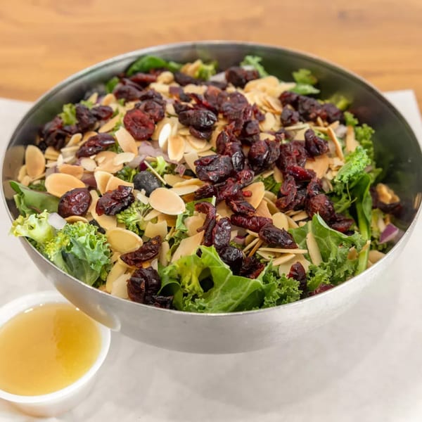 A large metal bowl of fresh green salad with dried cranberries and sliced almonds, with dressing on the side.
