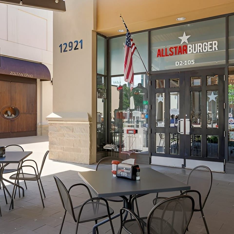 Outdoor patio seating with black tables and chairs in front of Allstar Burger restaurant.