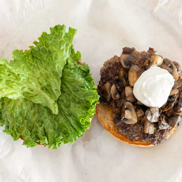 An open burger with lettuce on one bun and a patty with mushrooms and sour cream on the other.