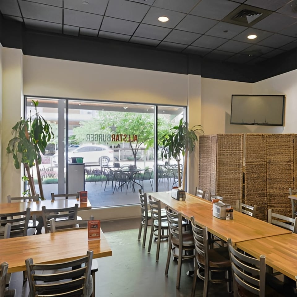 Interior of a restaurant with wooden tables, chairs, and large windows looking out onto a patio.