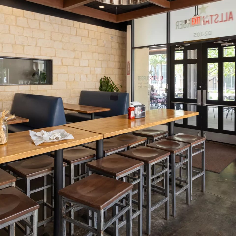 Interior of All Star Burger restaurant with high-top tables, stools, booth seating, and an entrance.